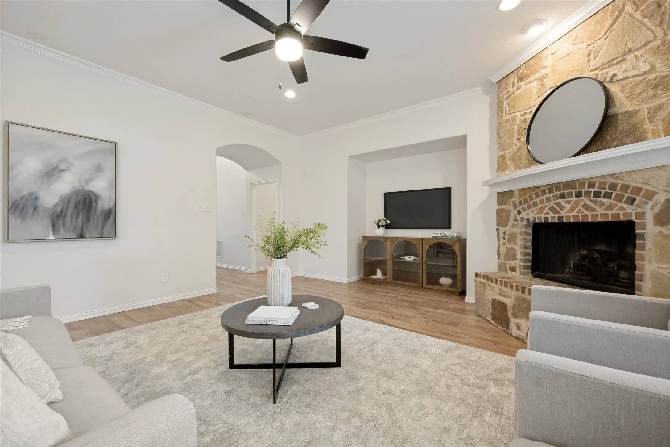 Living area featuring a stone fireplace with a brick firebox, wood-finish flooring, and white crown molding
