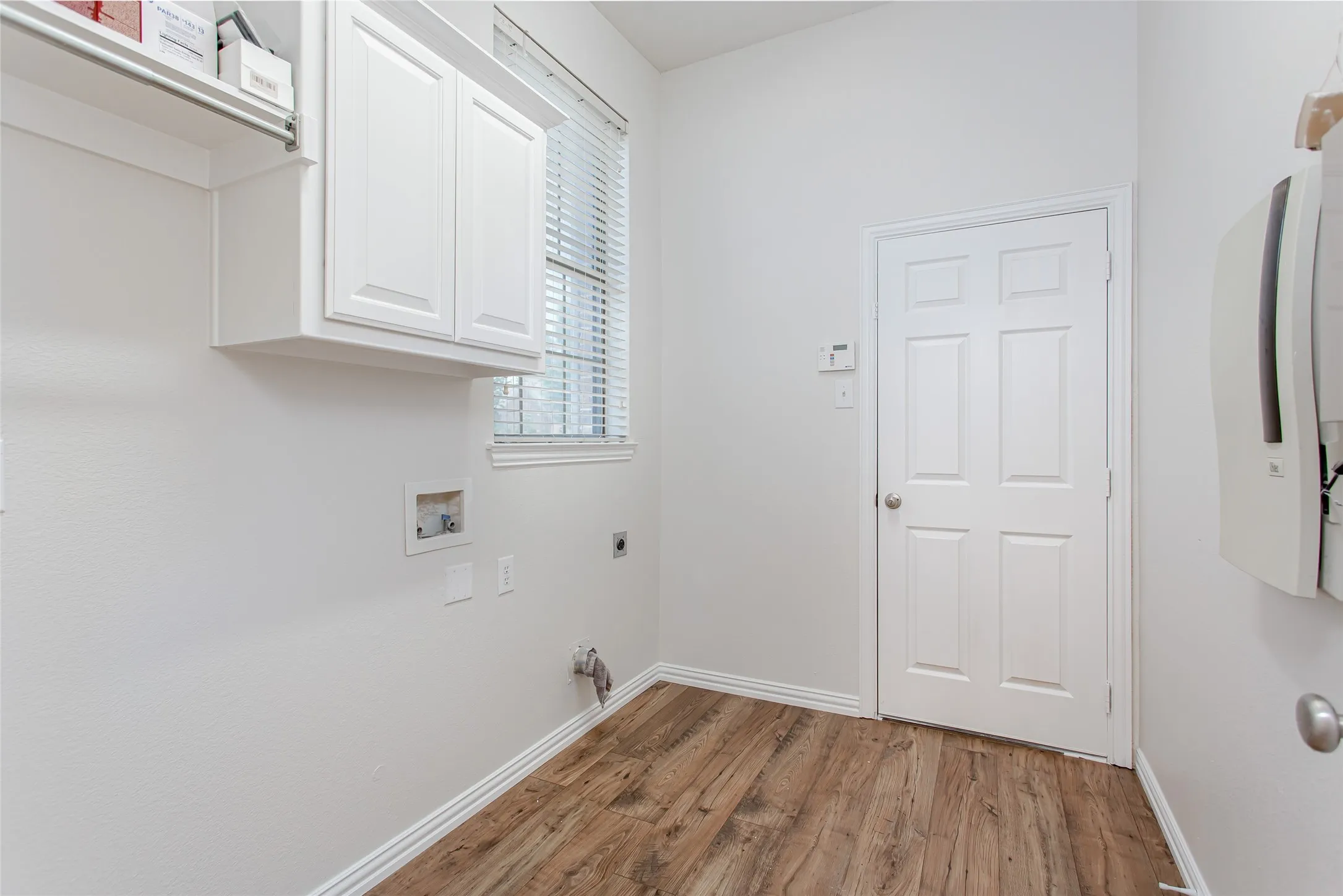 Laundry room featuring wood-finish flooring, white cabinetry, and a window with blinds