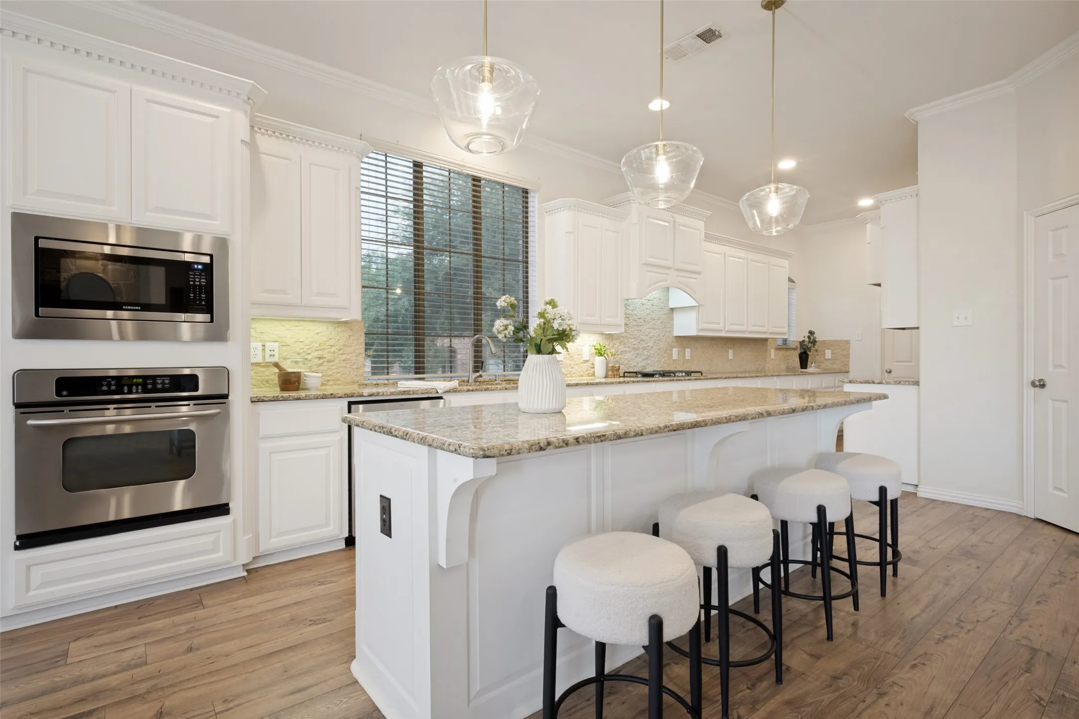 Gourmet kitchen featuring a large island with granite countertops, white cabinetry, stainless steel appliances, and wood-finish flooring