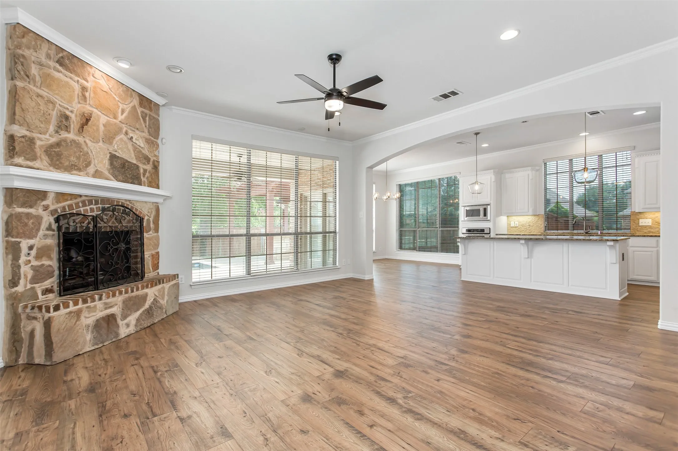 Spacious living area featuring wood-finish flooring and a stone fireplace with a brick hearth