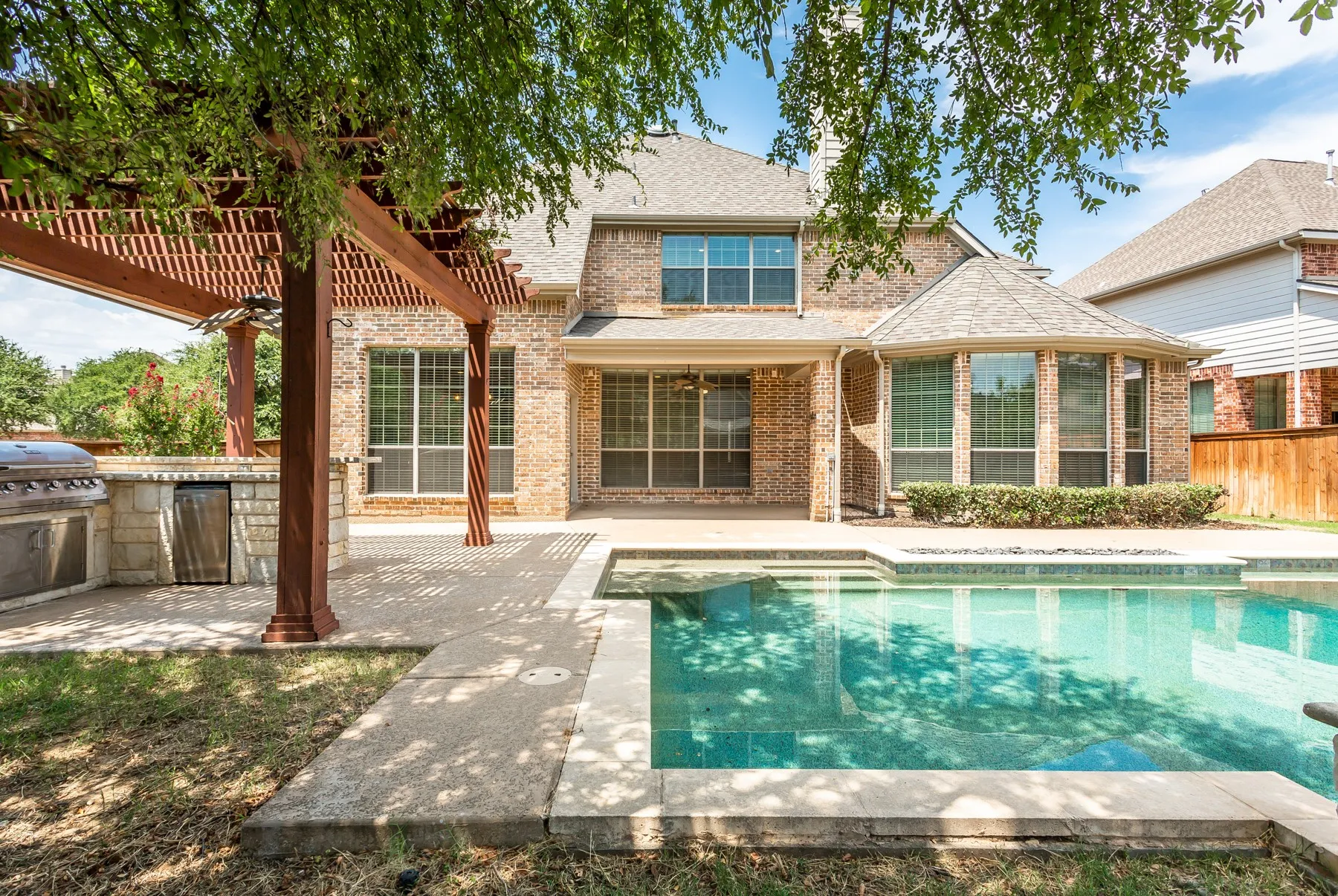 Backyard oasis featuring a swimming pool, covered patio and a pergola-covered outdoor kitchen with built-in grill and refrigerator