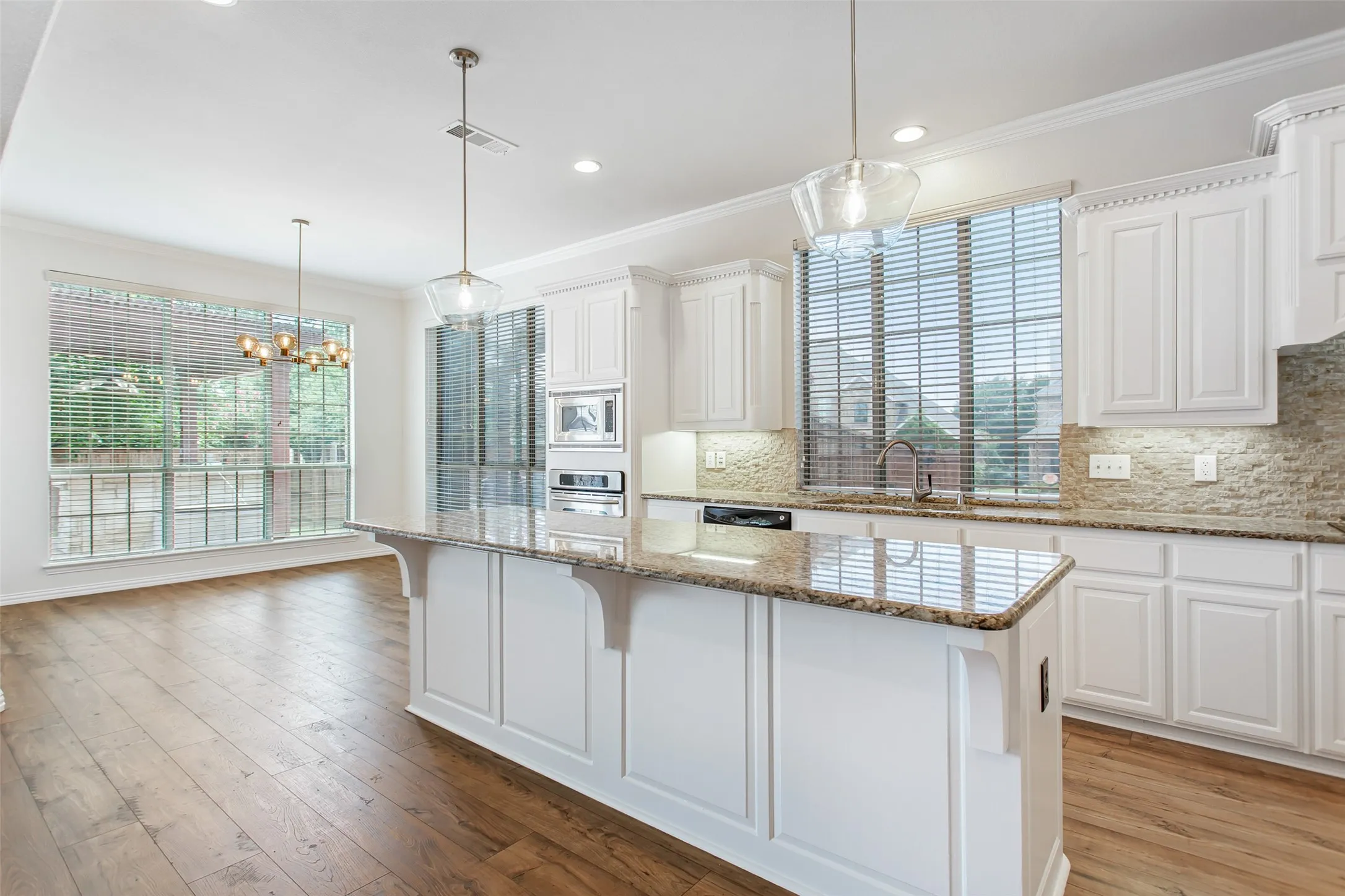 Kitchen featuring a center island with a granite countertop, white cabinetry, integrated stainless steel appliances, and a tiled backsplash