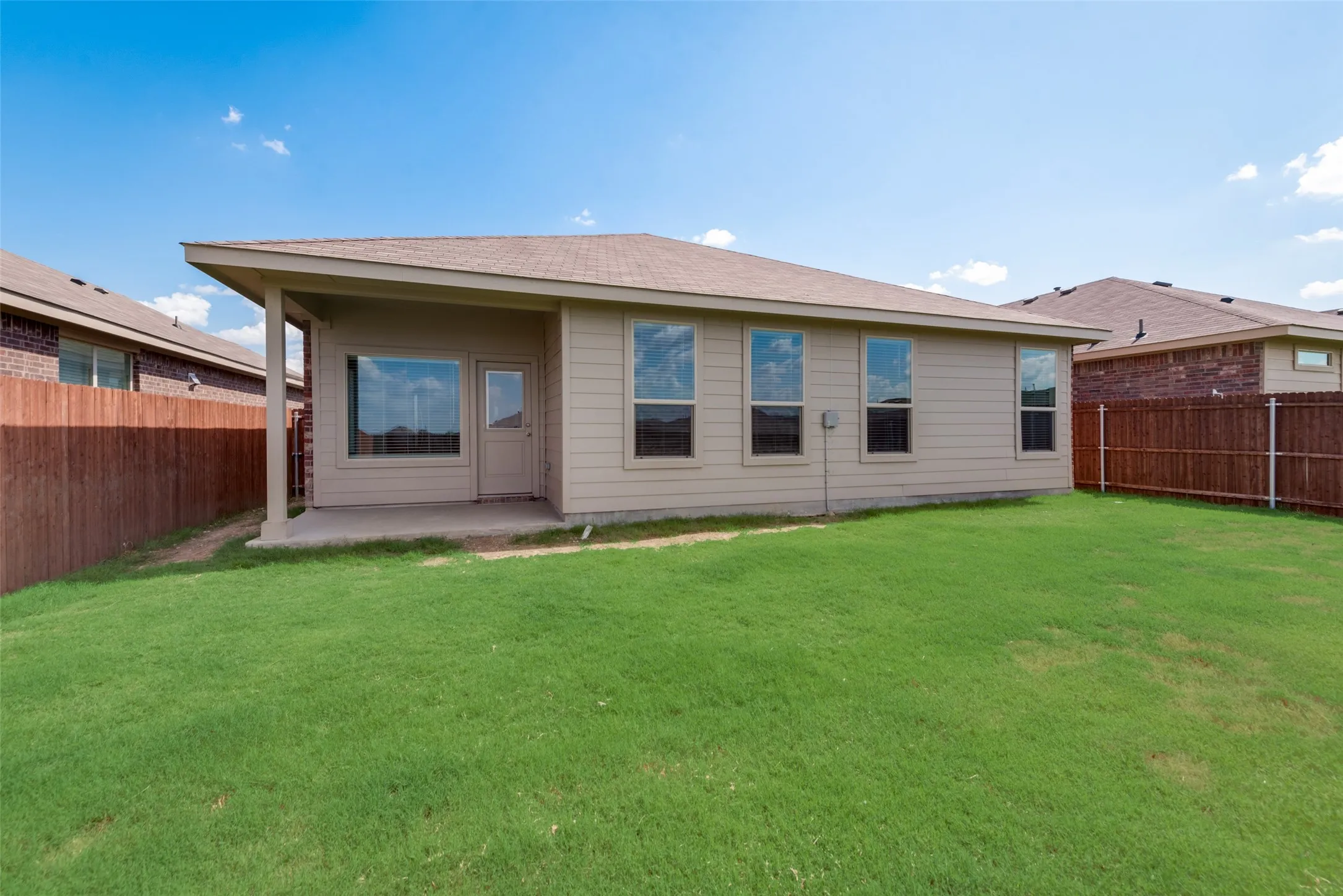 Expansive backyard featuring a covered patio, a privacy fence, and multiple windows along the rear exterior