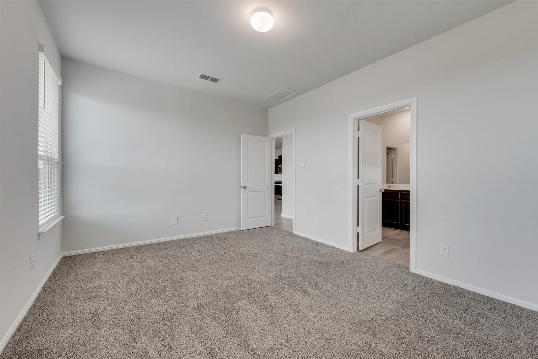 Carpeted room featuring a ceiling light fixture, white interior walls, and a window with horizontal blinds