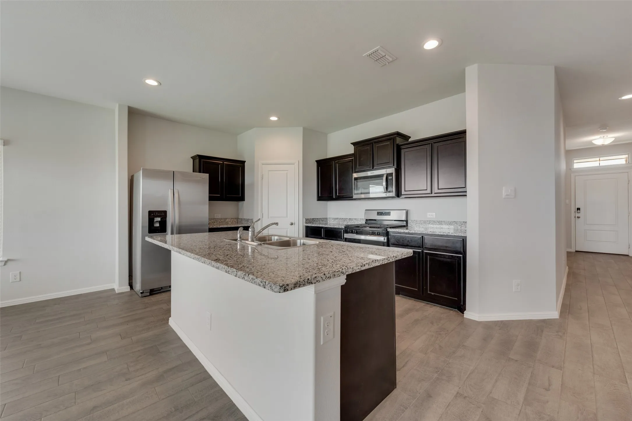 Kitchen featuring a central island with dual basin sink, granite countertops, dark wood cabinetry, and stainless steel appliances