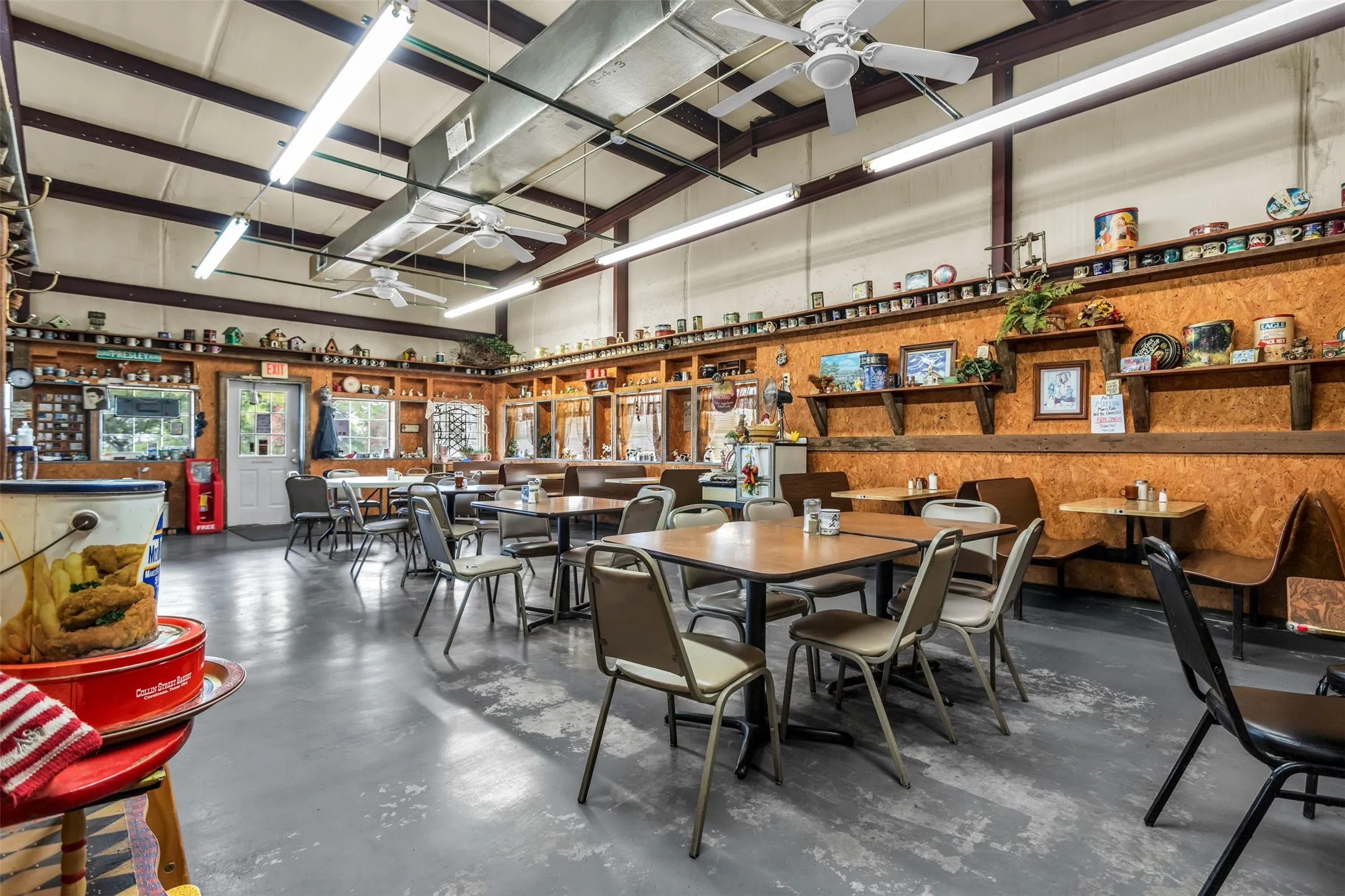 Spacious interior featuring a high ceiling with exposed beams, industrial fluorescent lighting, and multiple ceiling fans