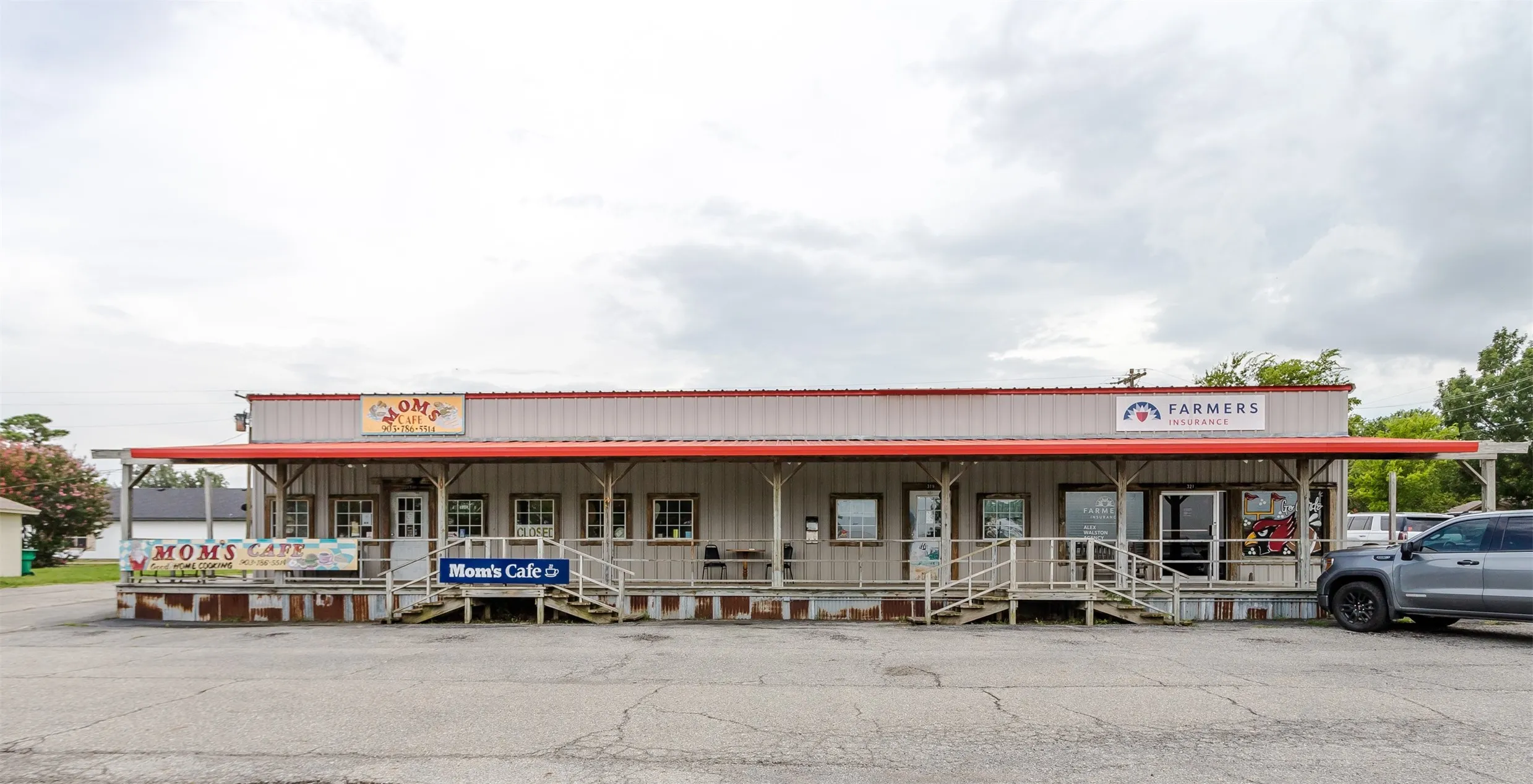 Single-story commercial building featuring a covered porch with multiple entry points, a light-colored metal exterior, and a red roof trim