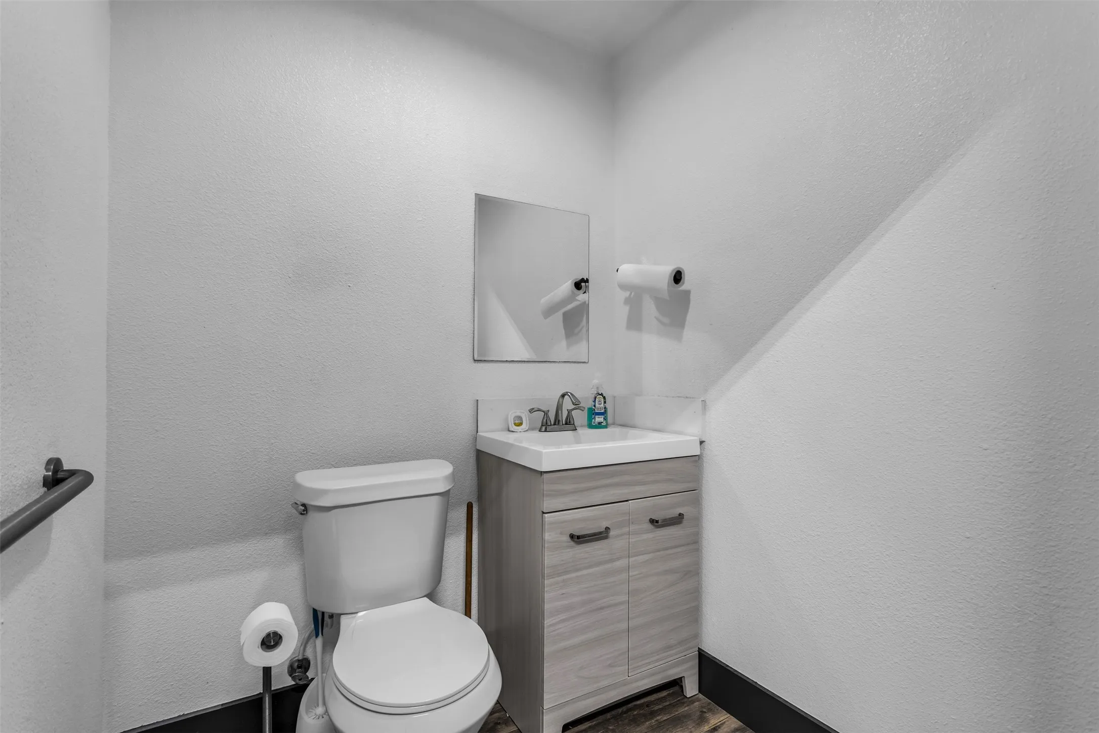 Bathroom featuring a light wood-finish vanity with a white countertop and rectangular sink, a wall-mounted mirror, and a grab bar