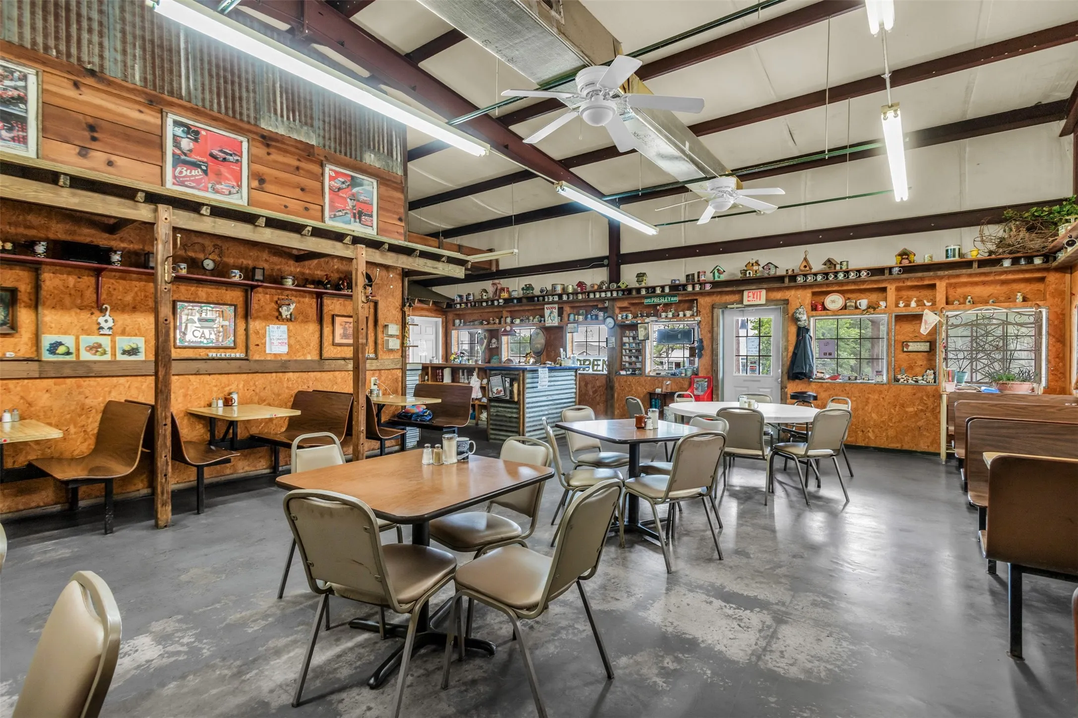 Spacious commercial interior featuring a high vaulted ceiling with exposed beams, multiple ceiling fans, and fluorescent lighting