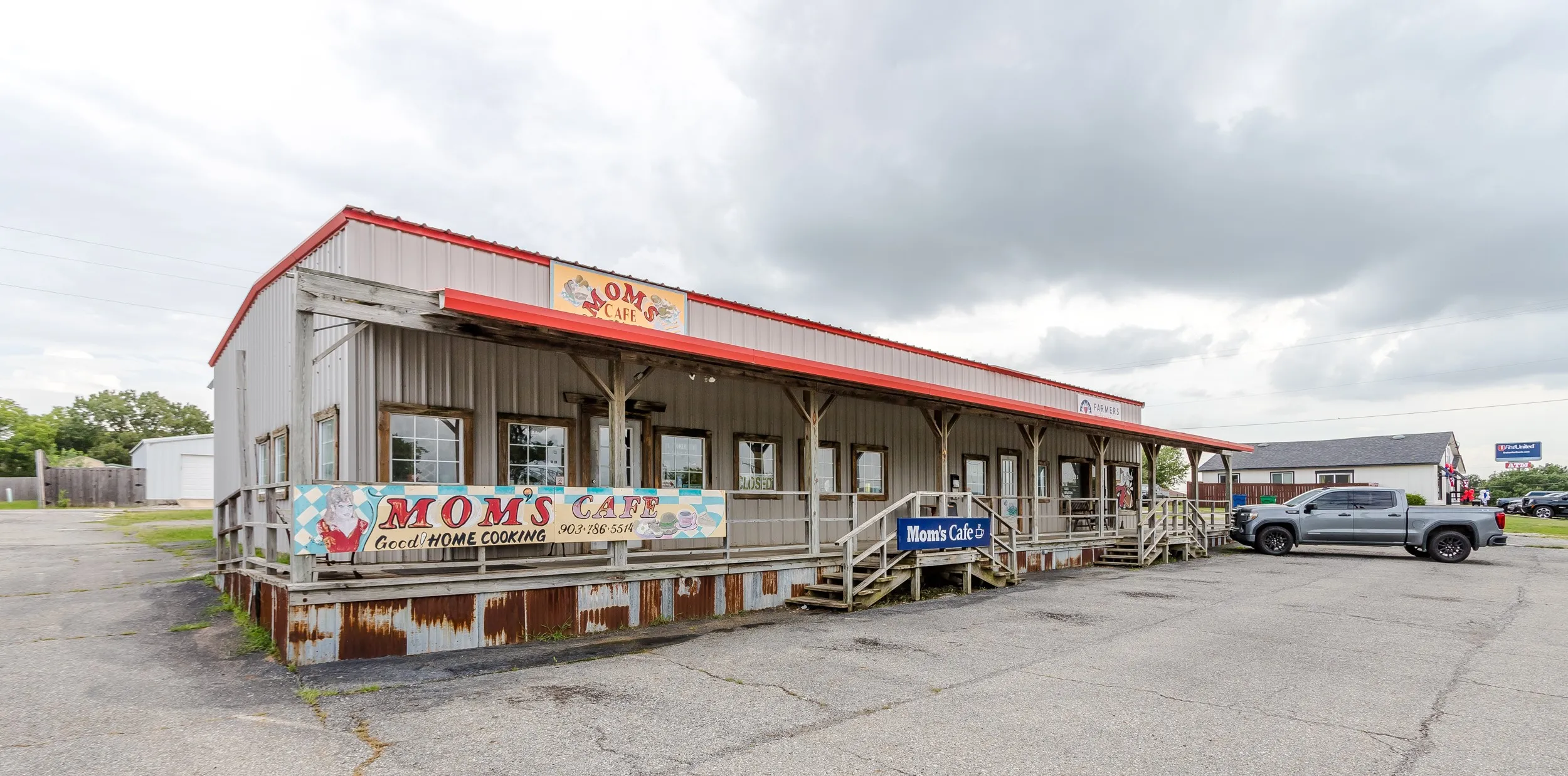 Commercial building featuring a red metal roof, covered front porch with railings, multiple large windows, and an asphalt parking area