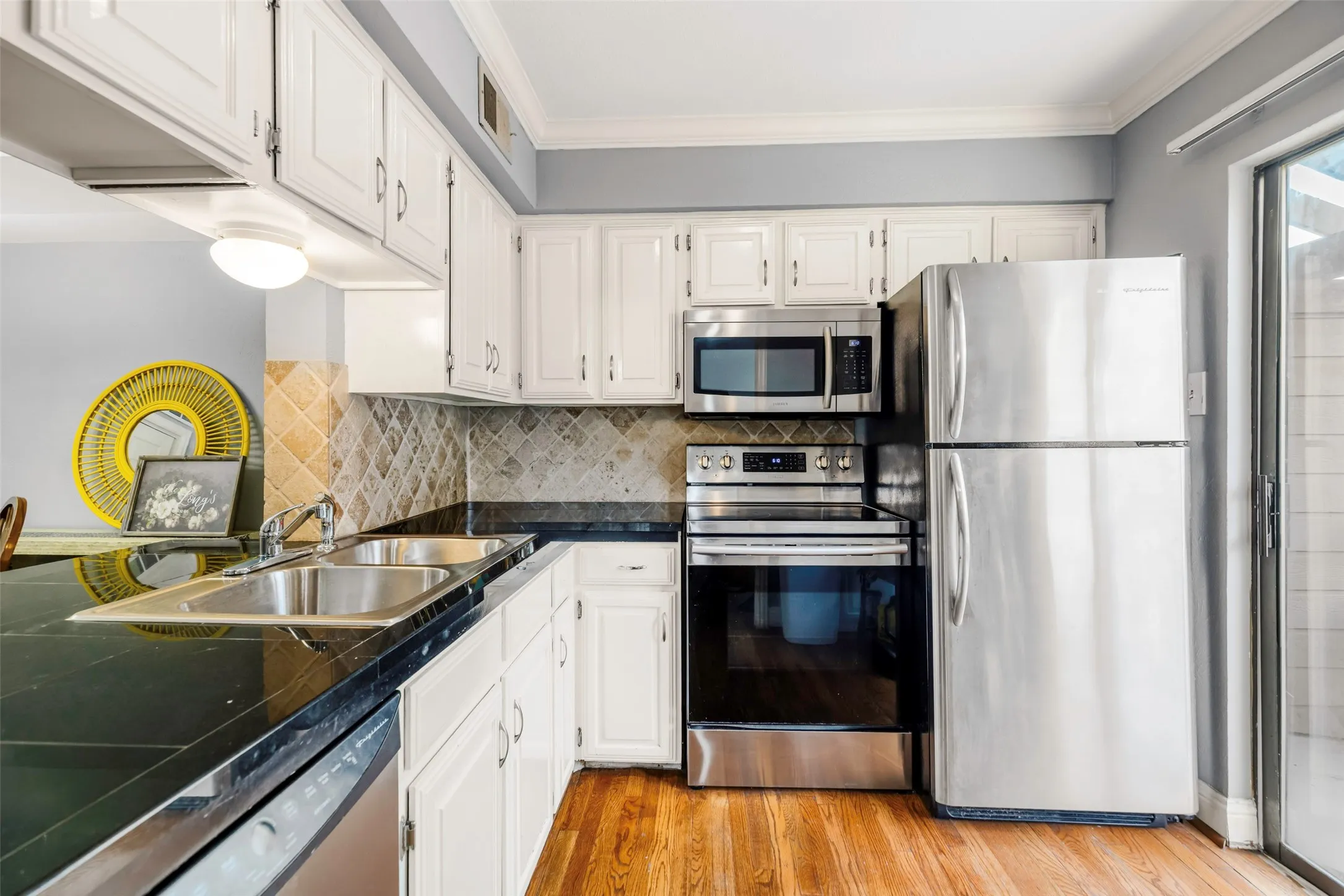 Kitchen featuring white cabinetry, black countertops, a stainless steel appliance suite, mosaic tile backsplash, and wood-finish flooring