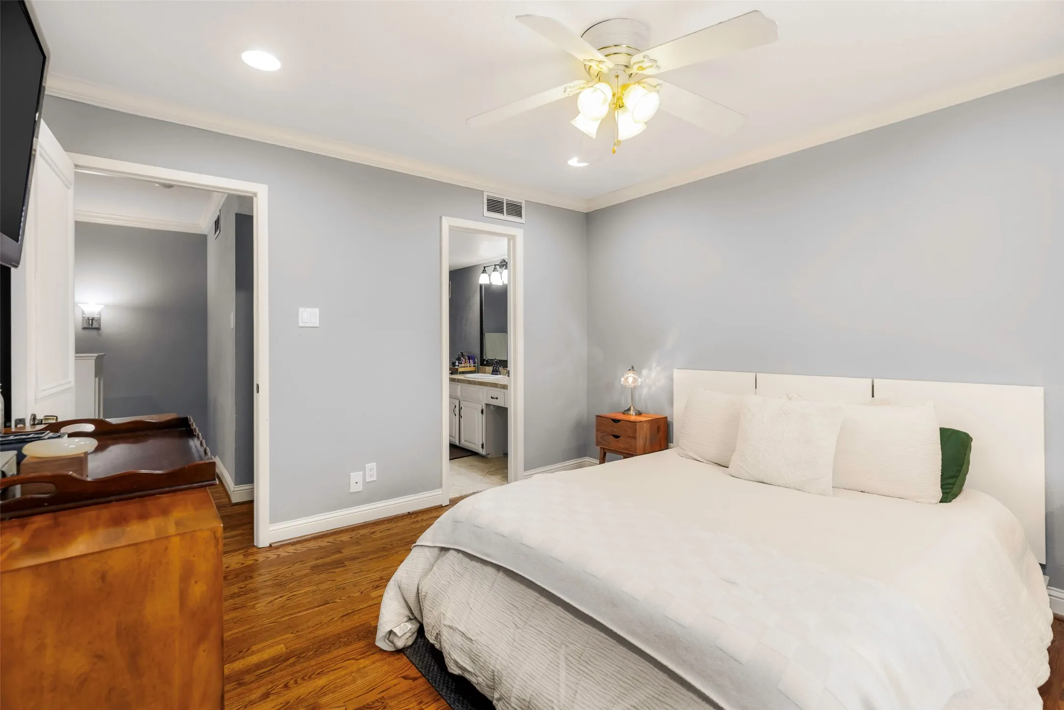 Bedroom featuring wood-finish flooring, light gray walls, white crown molding, and a ceiling fan with integrated lighting