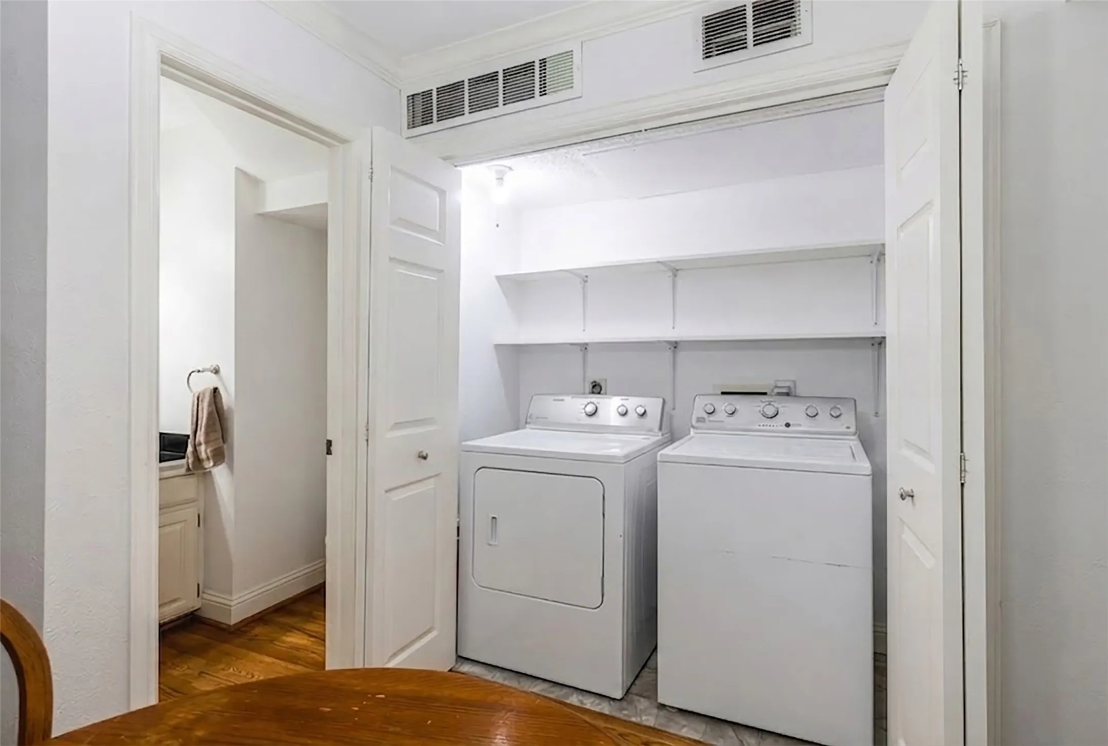 Dedicated laundry closet featuring a white washer and dryer, overhead shelving, and bi-fold doors