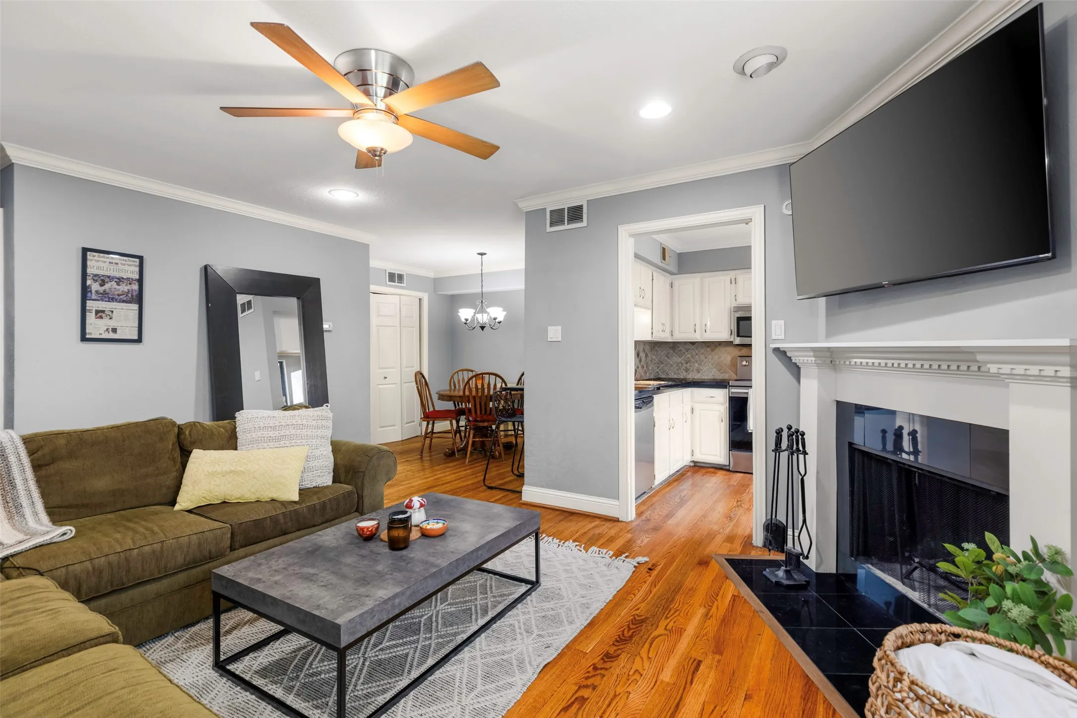 Living area featuring hardwood flooring, a ceiling fan with light, recessed lighting, crown molding, and a fireplace with a black tile hearth and white mantel