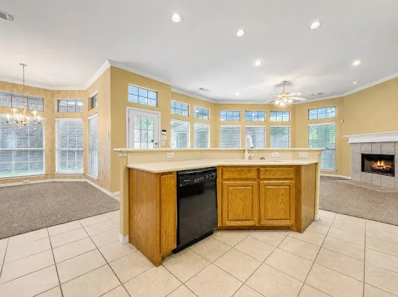 Open-concept kitchen featuring light wood cabinetry, a built-in dishwasher, and a breakfast bar with a neutral countertop