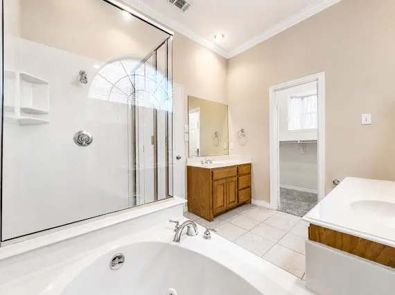 Bathroom featuring a built-in jetted tub, a separate glass-enclosed shower with an arched window, a vanity with a wood-finish base and integrated sink, and tile flooring