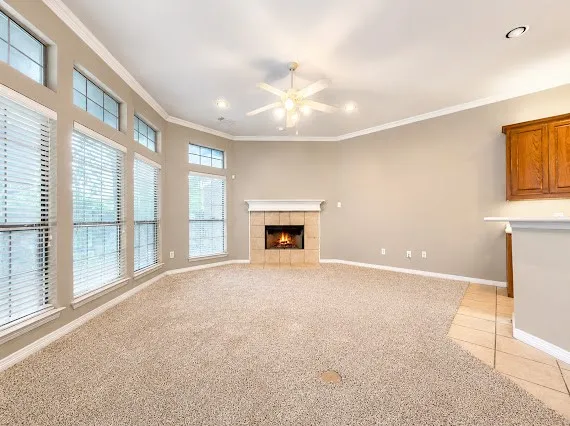 Spacious living area featuring a tile-surround fireplace with a white mantel, beige carpeting, and multiple large windows with blinds