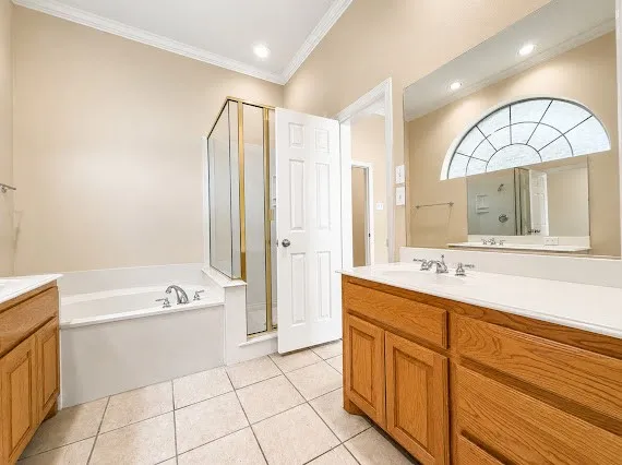 Bathroom featuring a soaking tub, glass-enclosed shower, dual wood-finish vanities with white countertops, and a decorative arched window