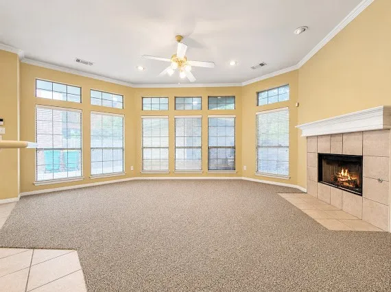Spacious living area featuring a bay window with multiple panes, a ceiling fan, recessed lighting, crown molding, and a tiled fireplace hearth