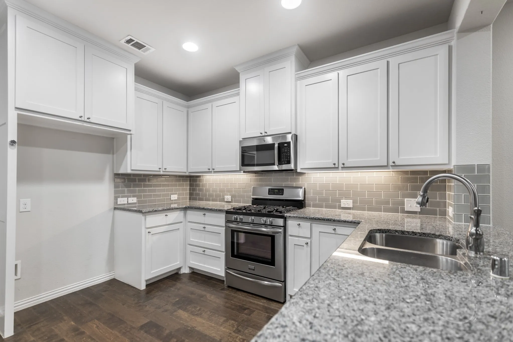 Modern kitchen featuring white shaker cabinetry, stainless steel appliances, granite countertops, subway tile backsplash, and wood-finish flooring