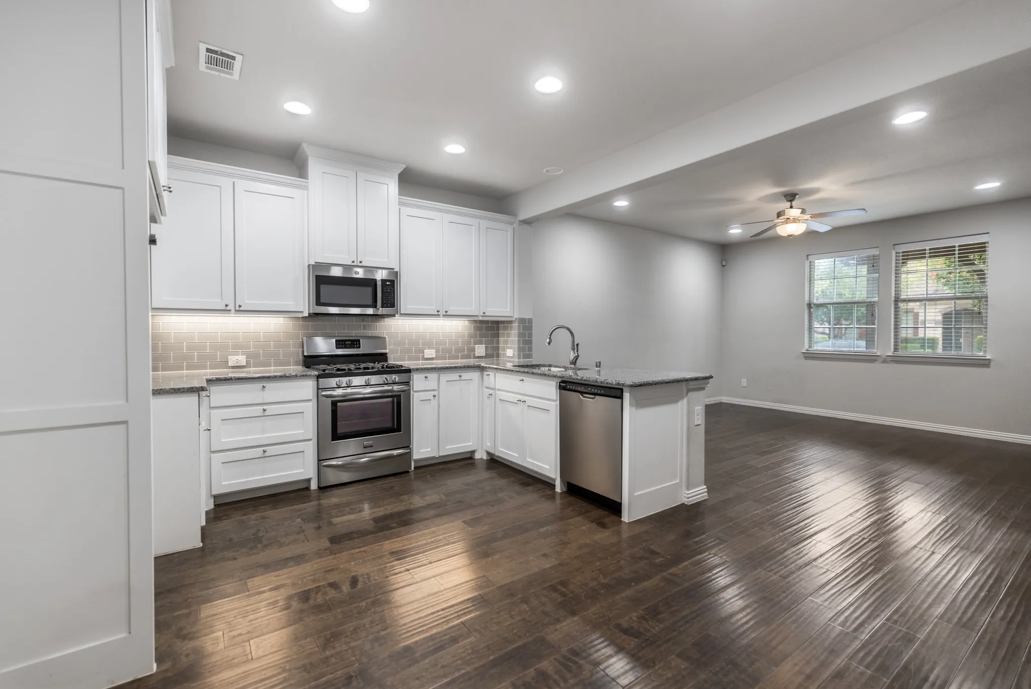 Modern kitchen featuring white shaker cabinetry, stainless steel appliances, granite countertops, and a subway tile backsplash