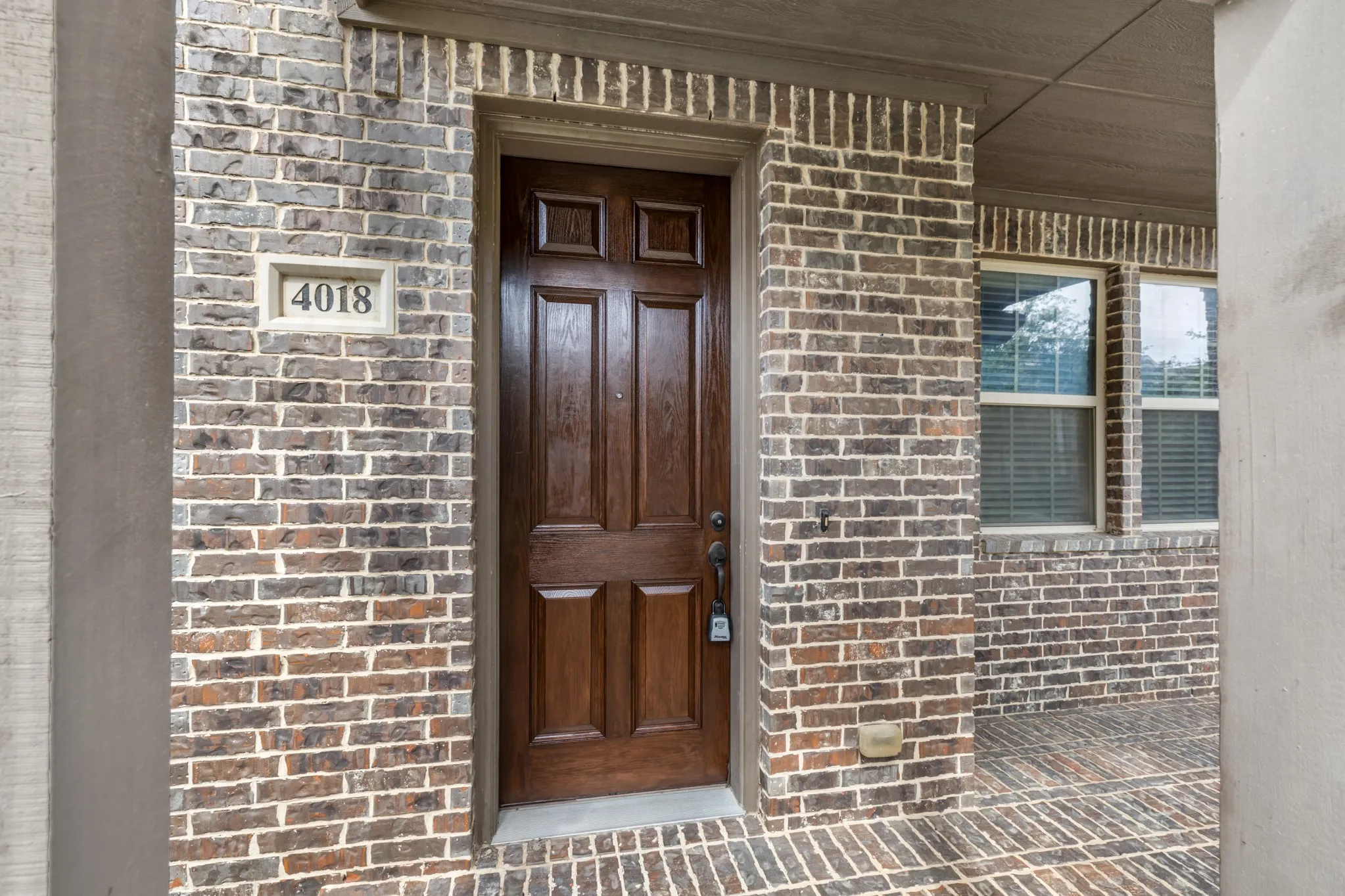 Entryway featuring a rich wood-finish panel door, multi-tone brick facade, and recessed address numbers