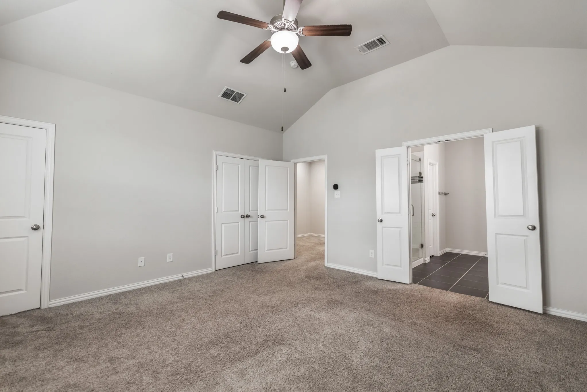 Spacious room featuring vaulted ceilings, neutral-toned carpeting, and a ceiling fan with integrated lighting