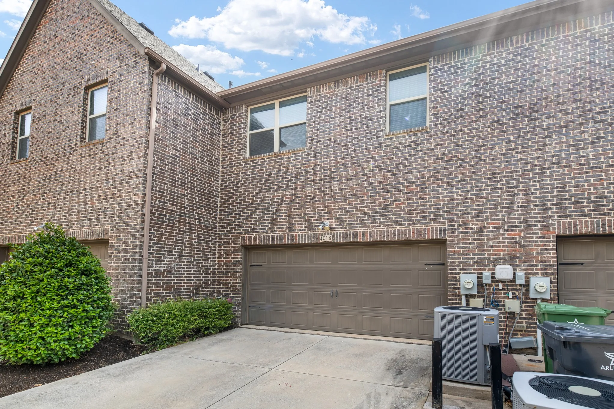 Brick exterior residence featuring multiple windows, a prominent garage door, and established landscaping