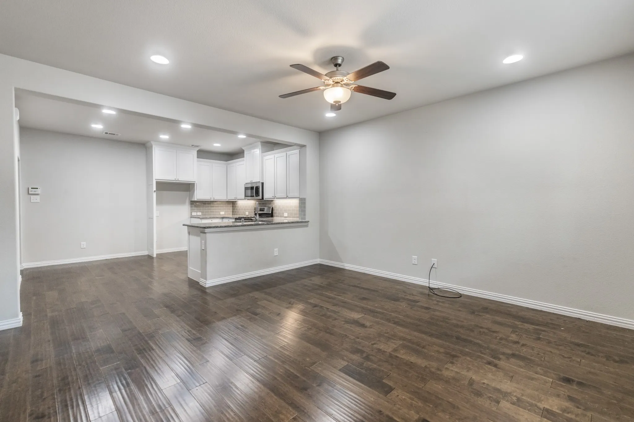 Open-concept living area with wood-finish flooring, a ceiling fan with integrated lighting, and recessed ceiling lights