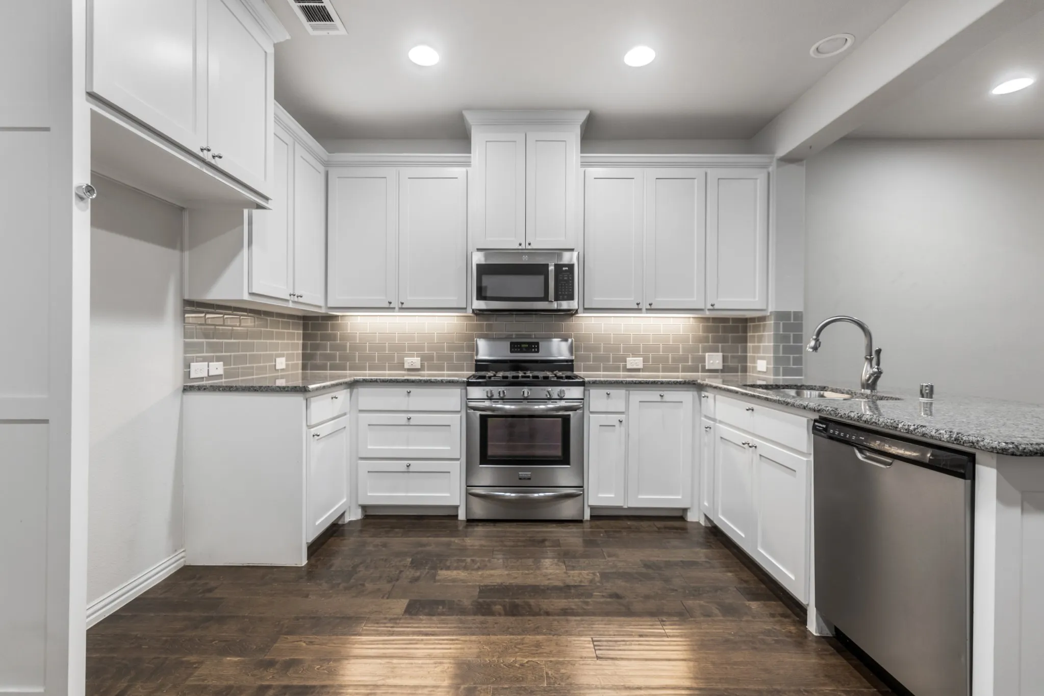 Kitchen featuring white shaker-style cabinetry, stainless steel appliances, granite countertops, and wood-finish flooring