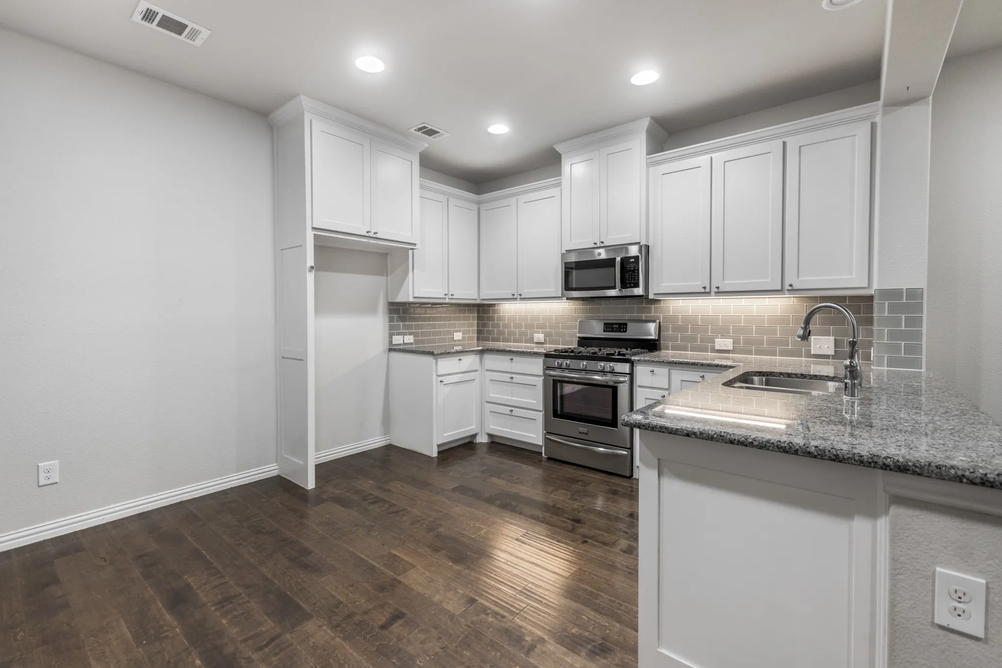 Kitchen featuring wood-finish flooring, white cabinetry, granite countertops, a subway tile backsplash, and stainless steel appliances