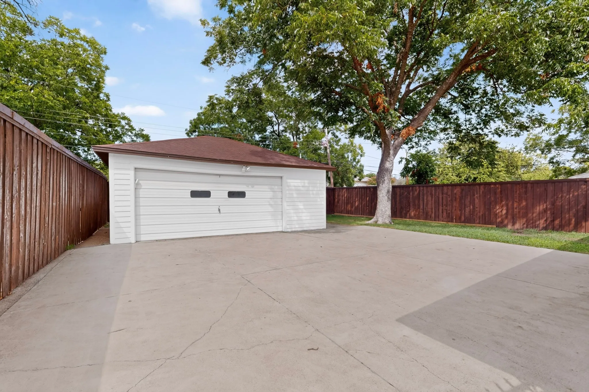 Detached garage with a white paneled door, concrete driveway, and brown privacy fencing