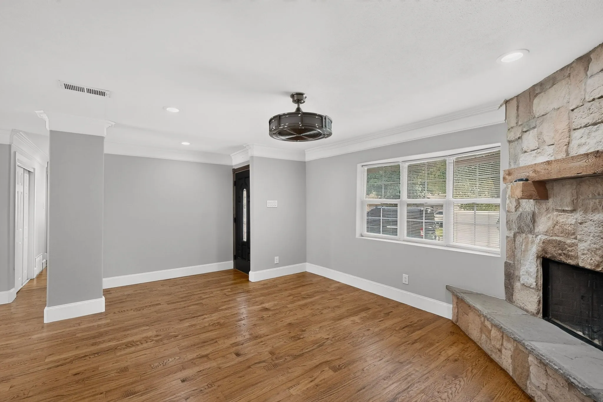 Spacious room featuring wood-finish flooring, a stone fireplace with a wood mantle, a dark entry door, and recessed lighting