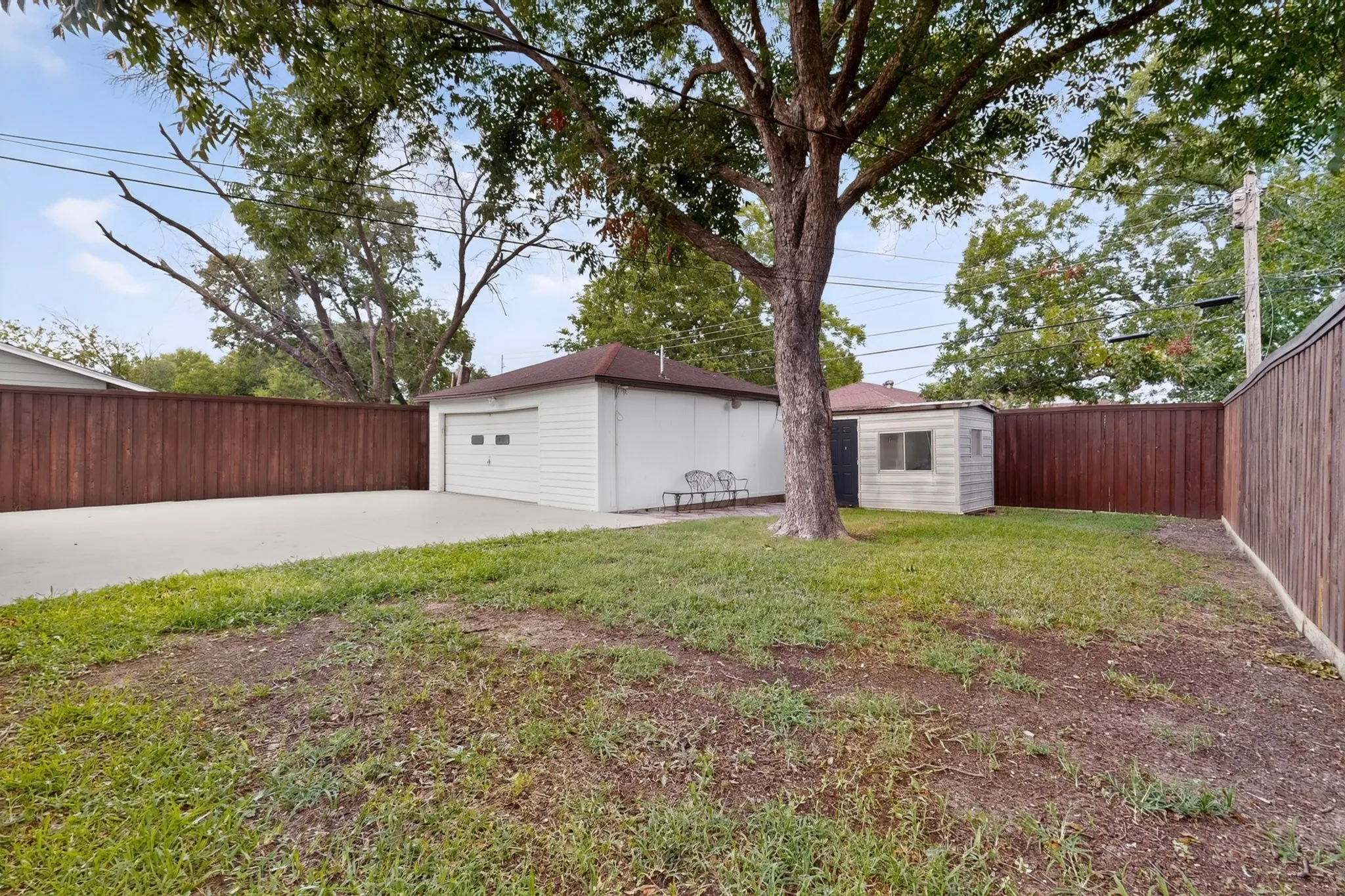 Spacious backyard featuring a detached garage, a storage shed, and a large tree