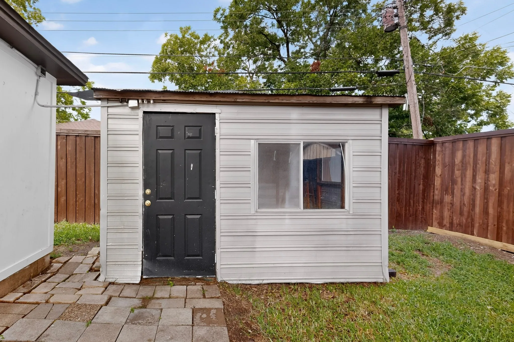 Detached shed featuring light-colored siding, a dark panel door, and a single window