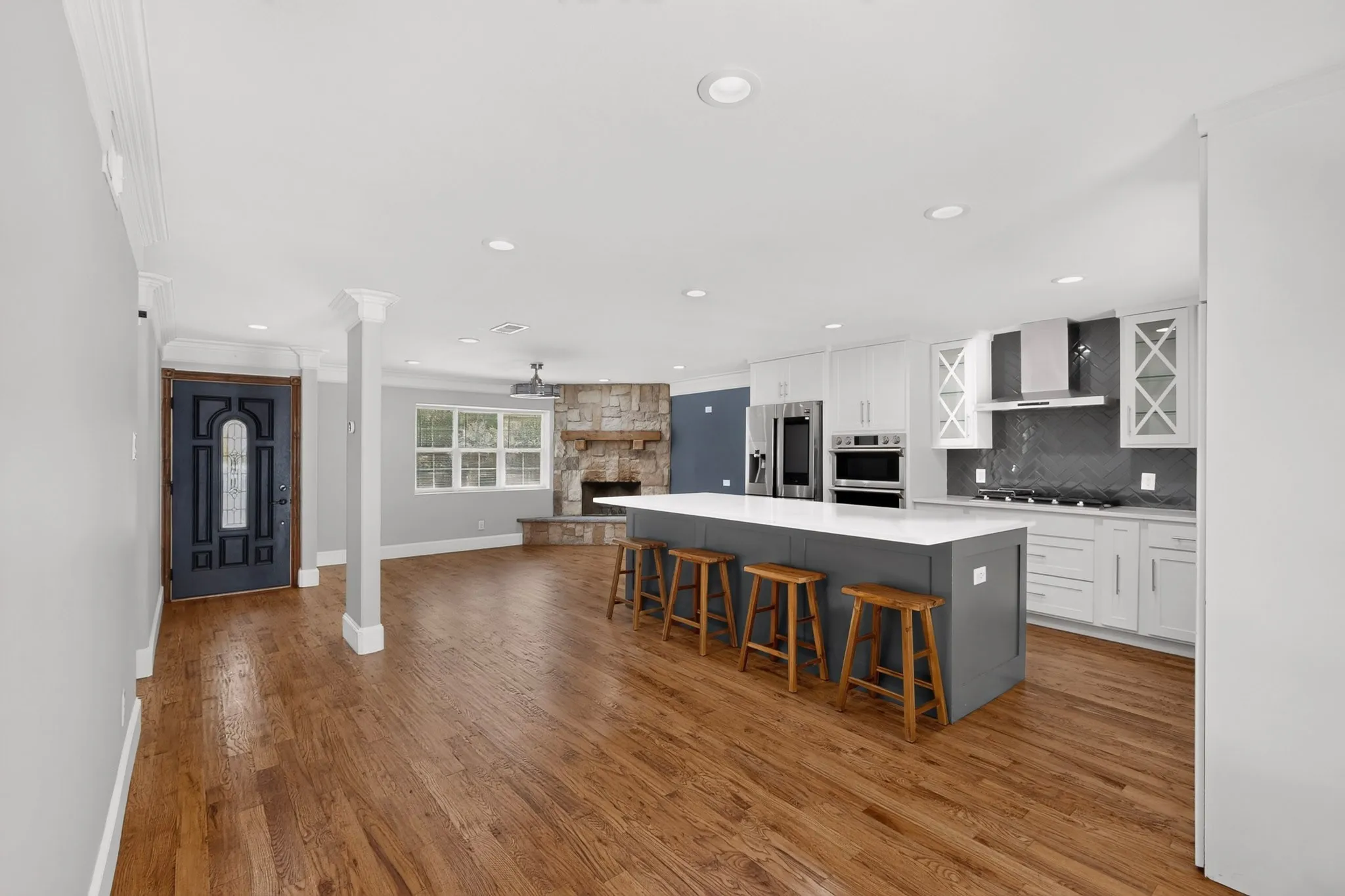 Open-concept living space featuring wood-finish flooring, a stone fireplace, and a kitchen island with seating