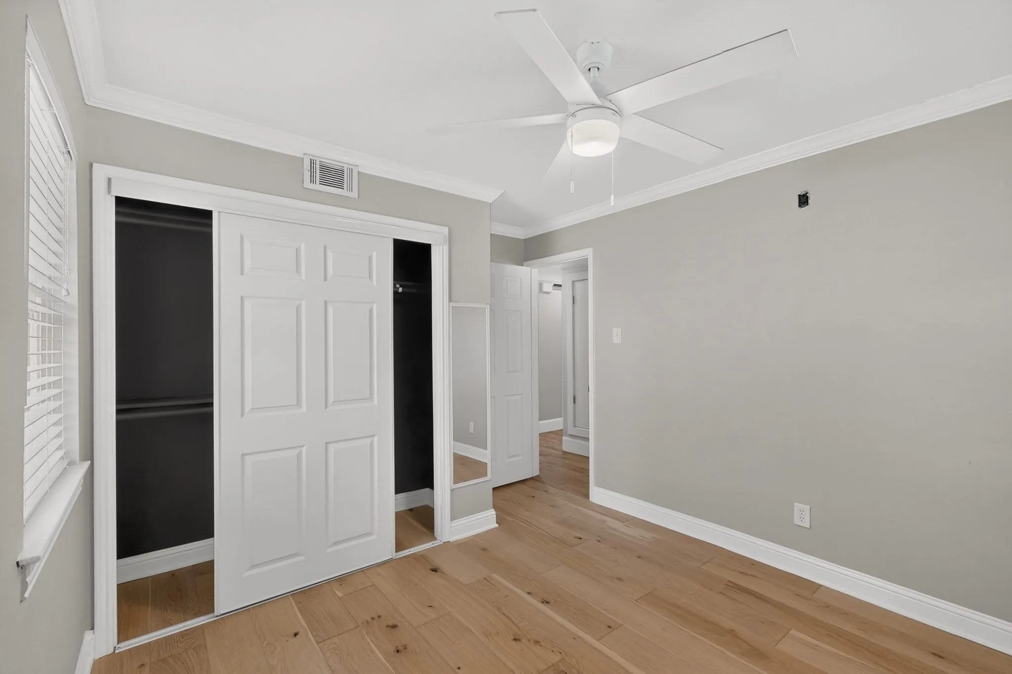 Bedroom featuring wide plank wood-finish flooring, a ceiling fan with integrated lighting, crown molding, and a sliding door closet with mirrored panels
