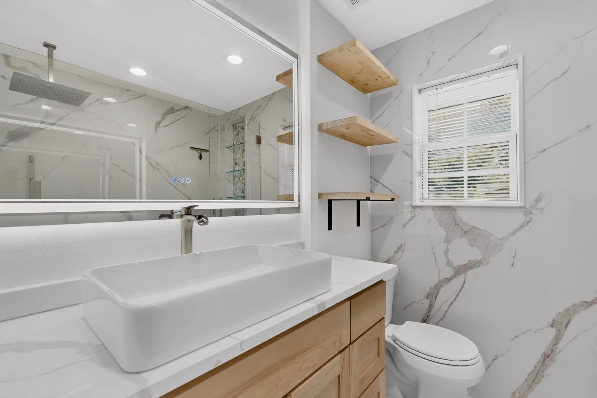 Modern bathroom featuring a rectangular vessel sink, wood-finish vanity, illuminated mirror, and a wall of marble-look tile