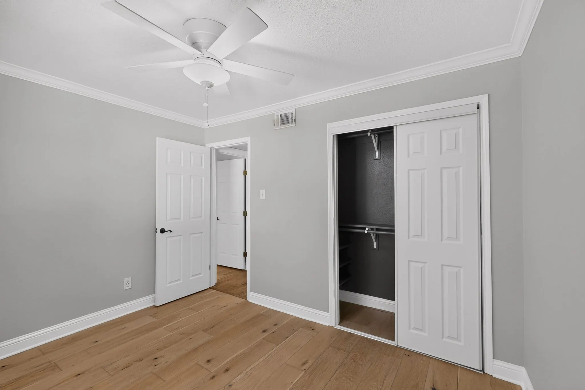 Room featuring wood-finish flooring, light gray walls, a white ceiling fan, and crown molding