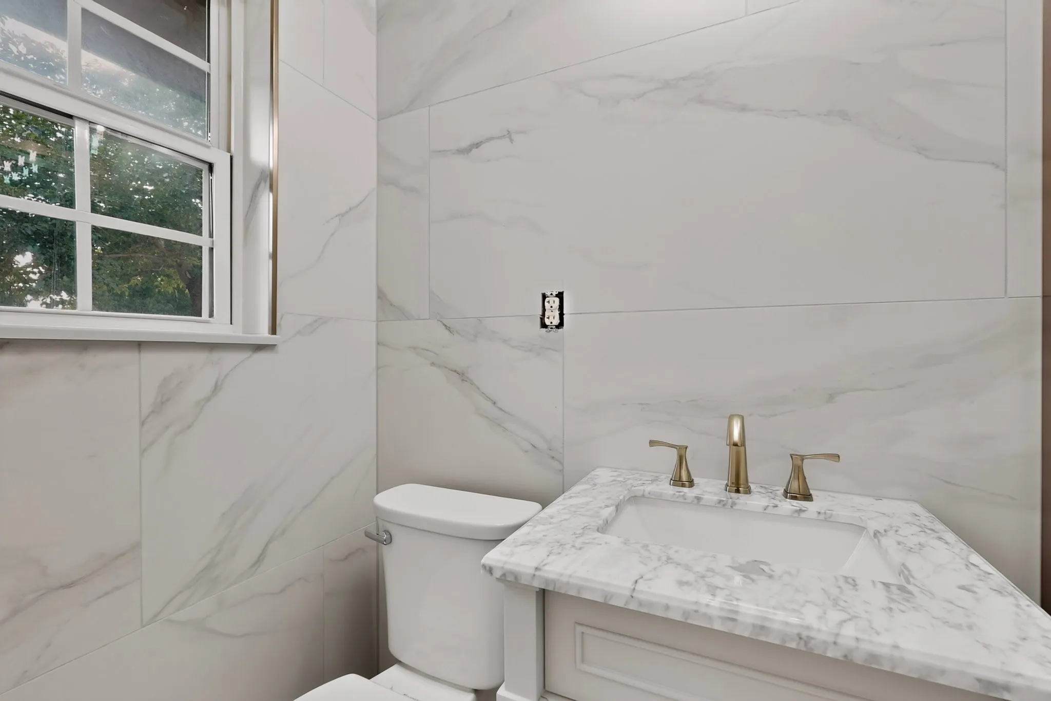 Contemporary bathroom featuring large format marble-look wall tiles, a white vanity with a marble-look countertop, an integrated rectangular sink, and gold-toned fixtures