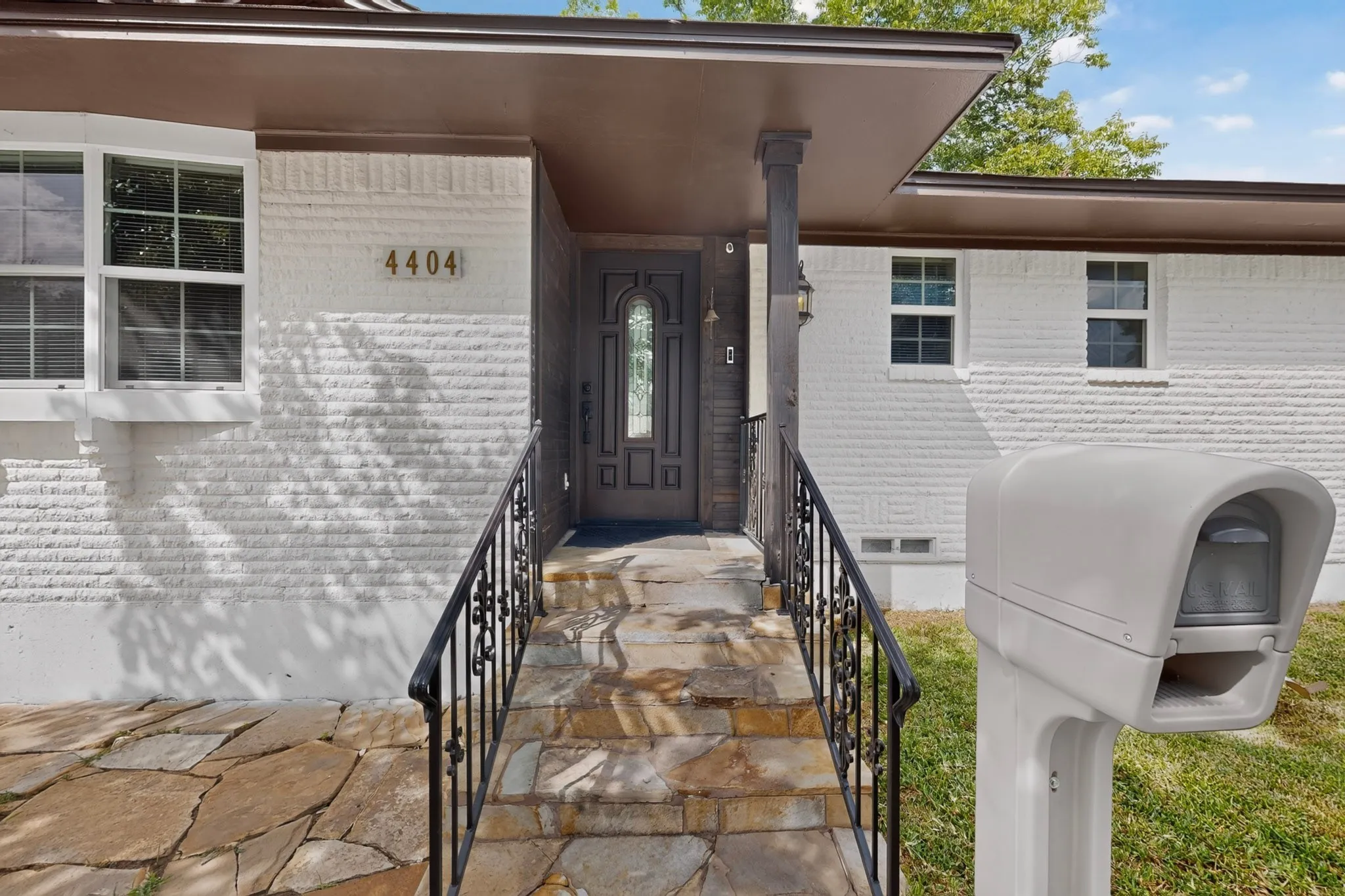 Stone walkway leading to a covered entry with a dark wood door featuring decorative glass