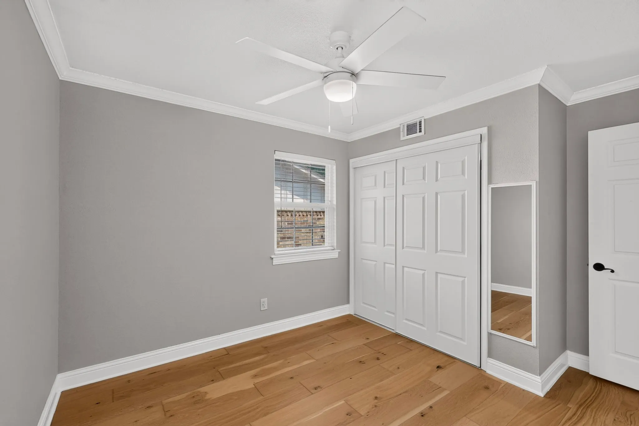 Room featuring wood-finish flooring, light grey painted walls, white crown molding, and white baseboards