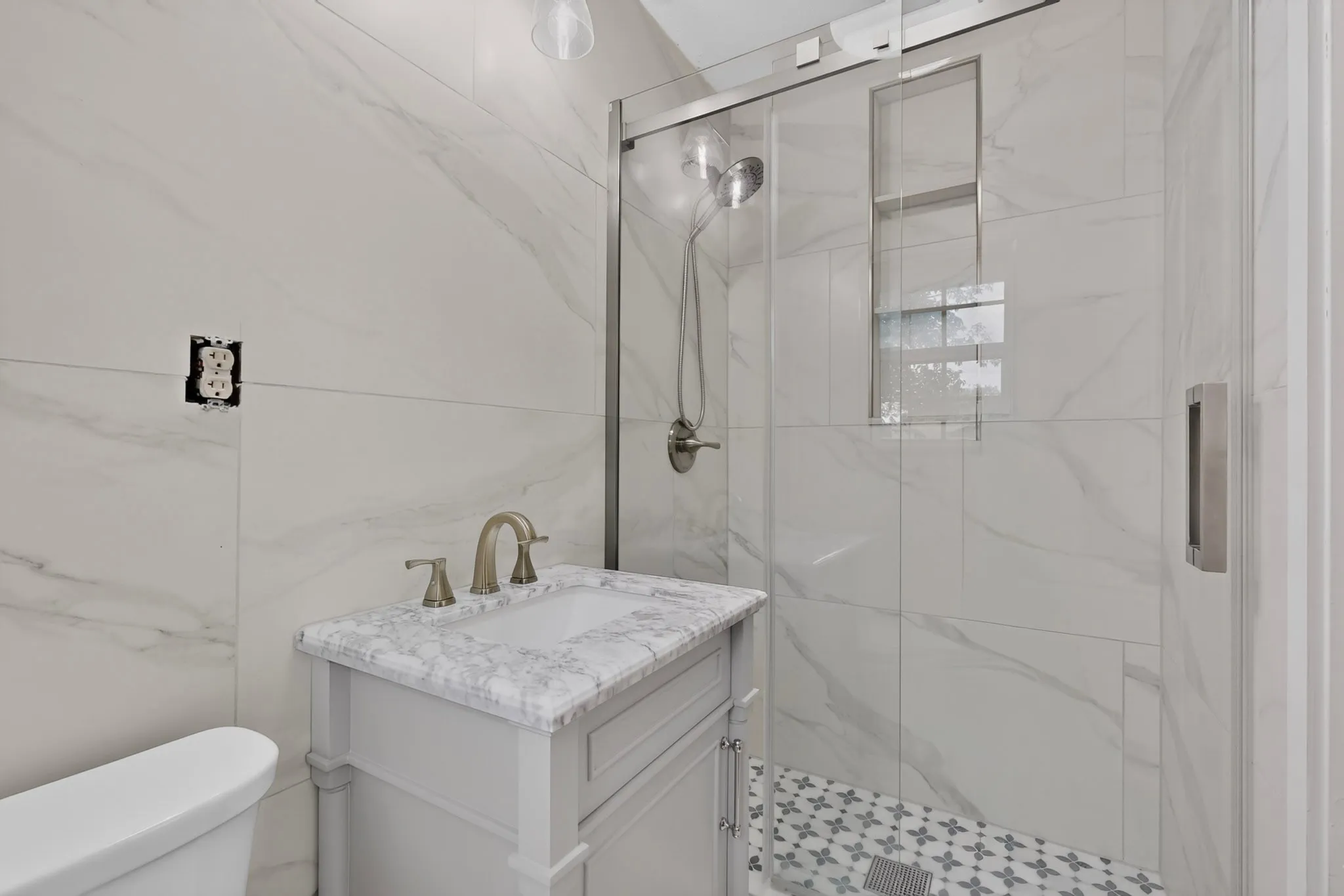 Contemporary bathroom featuring a glass-enclosed shower with a recessed niche, patterned tile flooring, and a vanity with a stone countertop