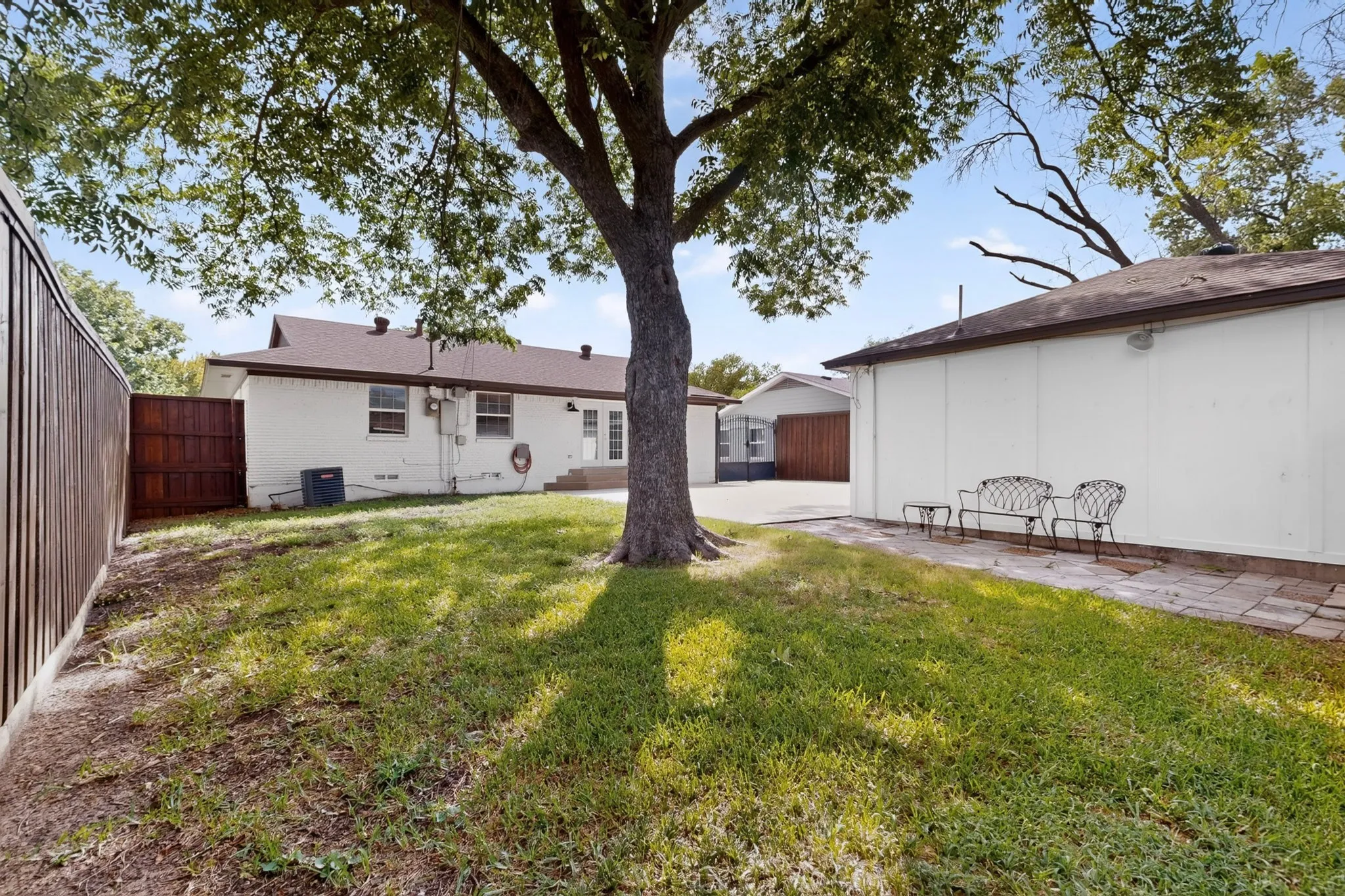 Expansive lawn area featuring a mature tree, perimeter fencing, a paved patio section, and a white-painted rear exterior