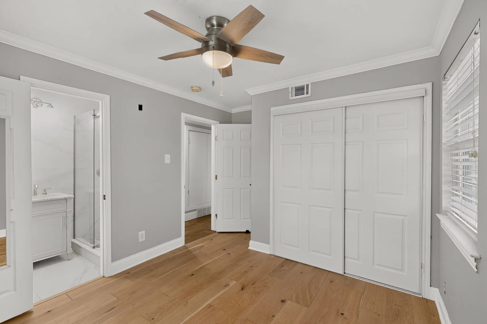 Spacious room with wood-finish flooring, white baseboards, and white crown molding