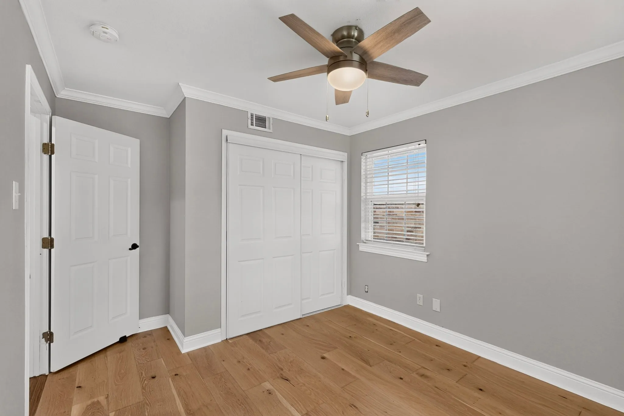 Room featuring wood-finish flooring, a ceiling fan with light fixture, and a window with blinds