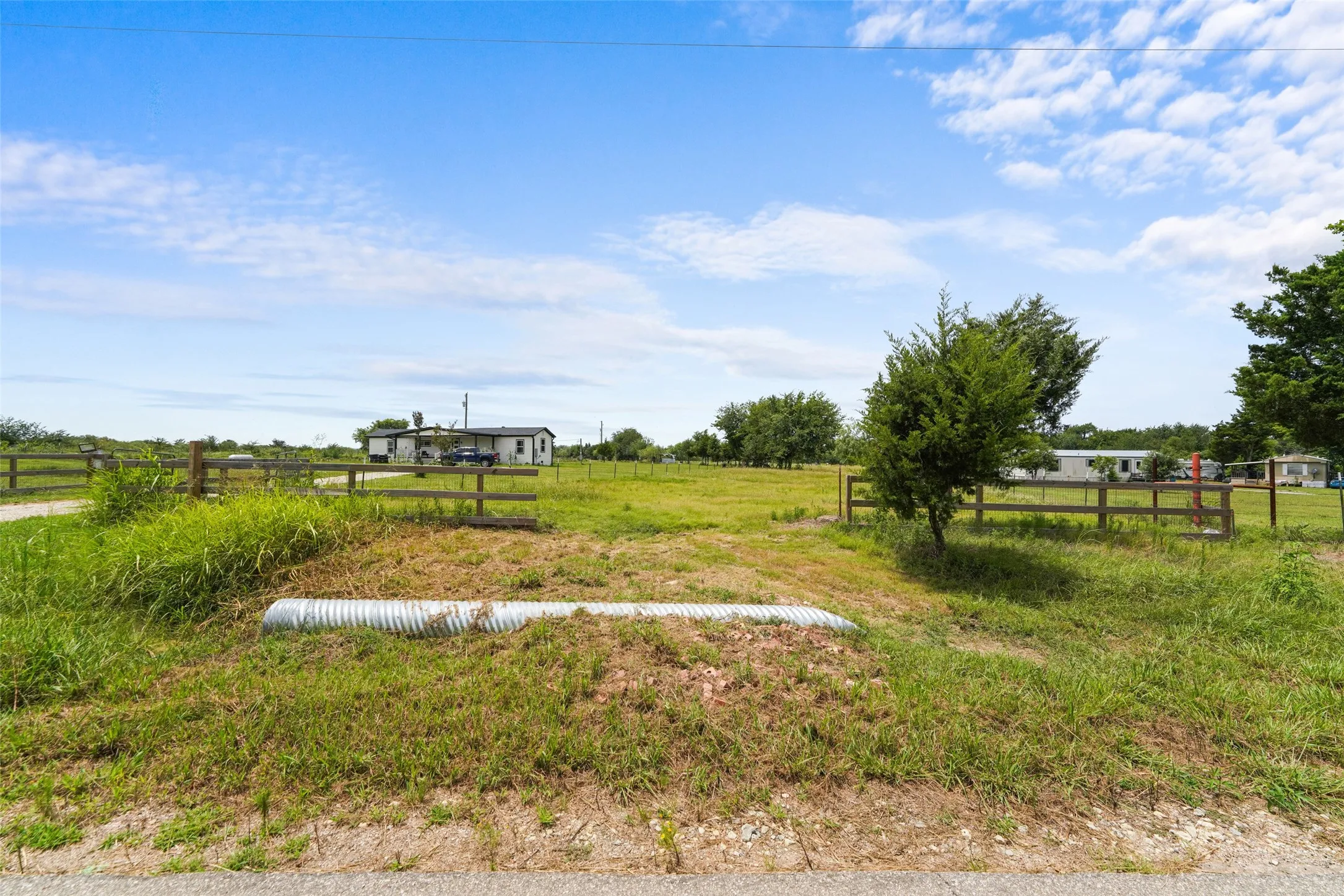 Expansive open land featuring a wooden fence boundary, scattered mature trees, and a visible culvert