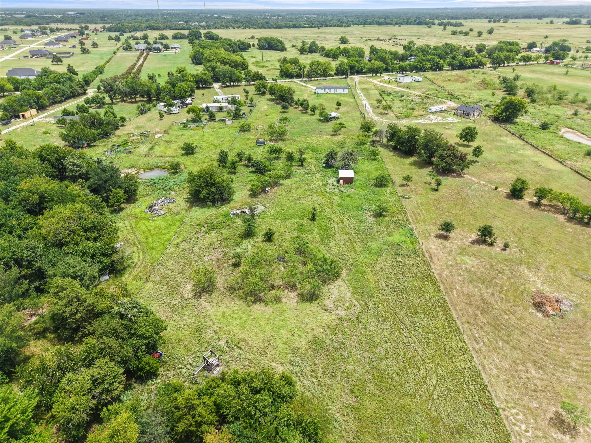 Expansive green acreage featuring scattered trees, a small pond, and a detached outbuilding