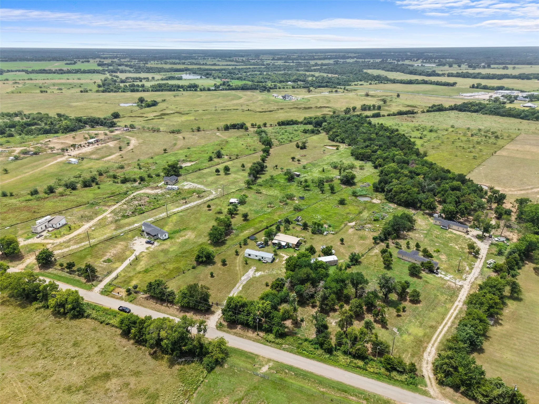 Expansive rural landscape featuring scattered residences, mature trees, and a distant body of water