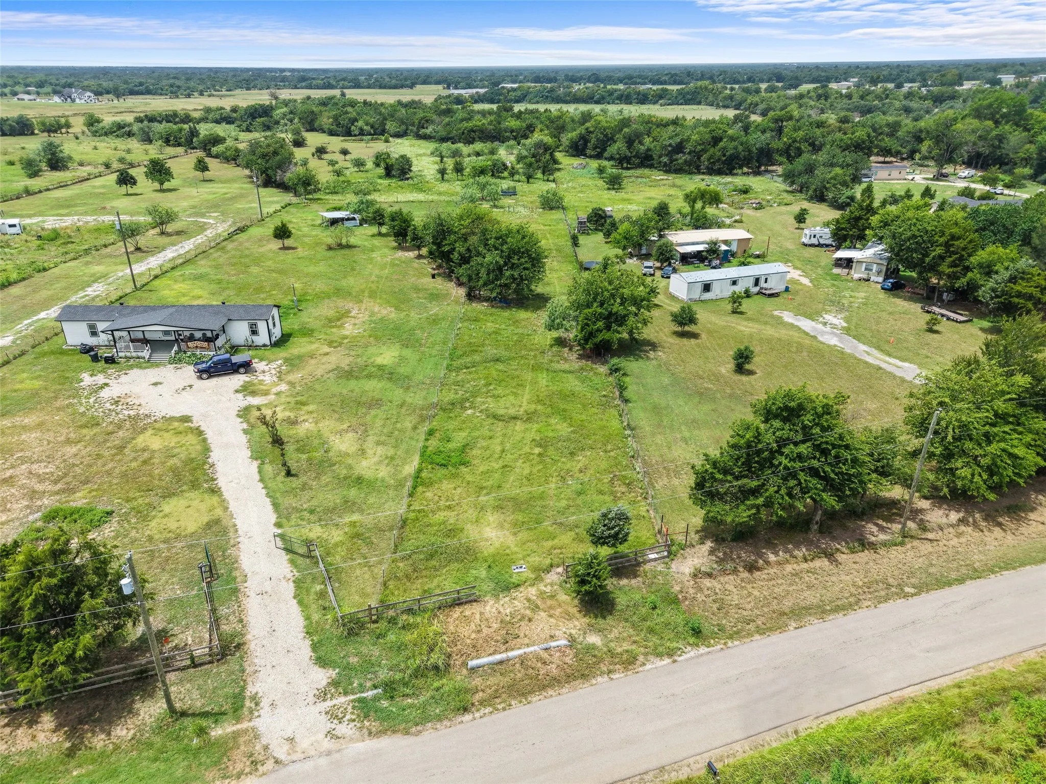 Expansive rural property featuring a gravel driveway, mature trees, and open green spaces